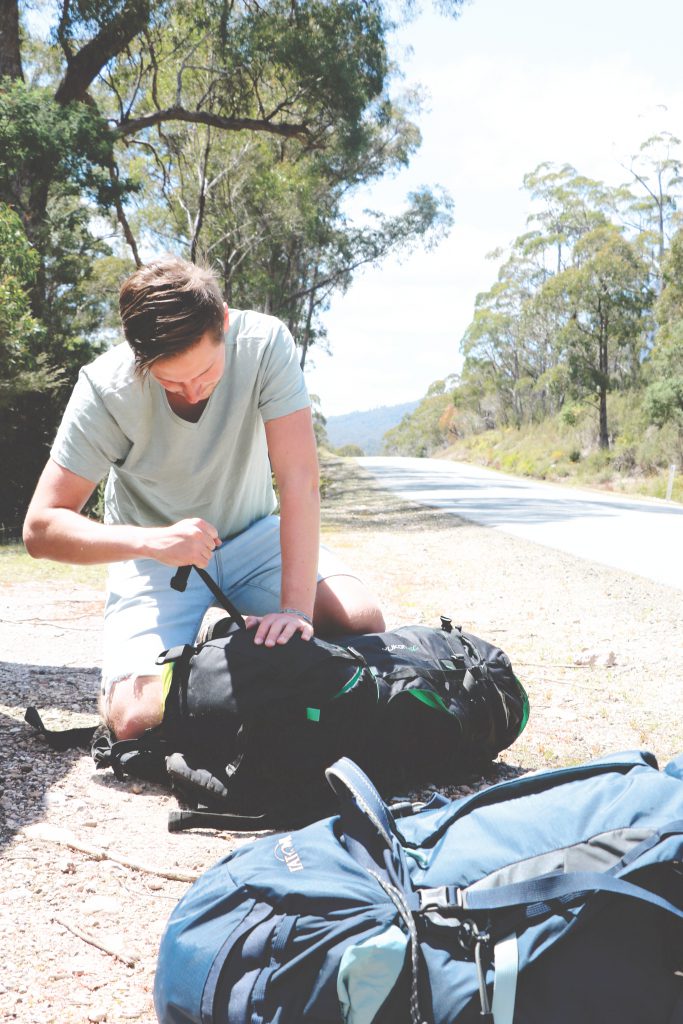 Daniel kniet am Straßenrand vor dem Nationalpark auf Tasmanien und packt seinen Tatonka Yukon Trekkingrucksack.
