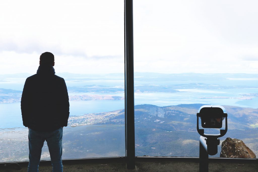 Auf dem Gipfel des Cradle Mountain: Daniel schaut mit einem Rundumblick auf die unten liegenden Seen und Wanderwege des Cradle-Mountain-Lake-St.-Clair-Nationalparks auf Tasmanien.