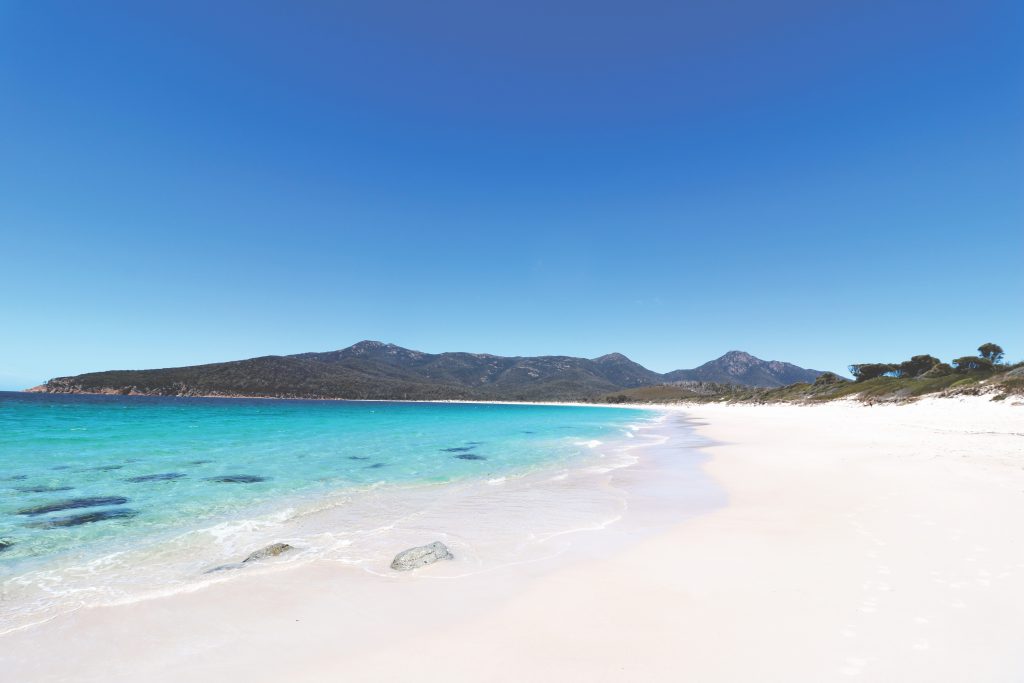 Ganz nah dran: Ania und Daniel (nicht im Bild) direkt am Ufer der Wineglass Bay Bucht auf Tasmanien. Vor ihnen das türkisblaues Wasser des Meeres.