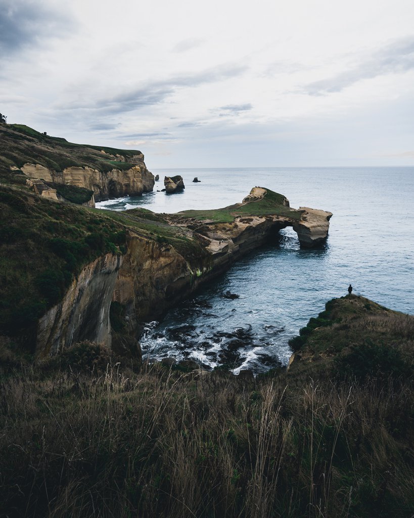 Hannes Stier blickt auf einen Felsbogen am Tunnel Beach bei Dunedin.