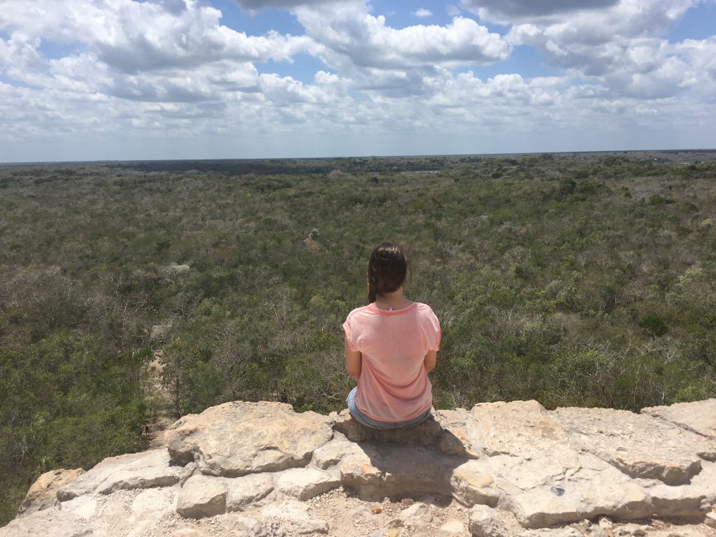 Roadtrip Yucatan - Sophie sitzt auf der Nohoch Mul Maya-Pyramide und blickt auf den umliegenden Dschungel der Ruinenstätte Coba in Mexiko.