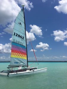 Roadtrip Yucatan - Ein Katamaran-Boot mit buntem Segel ankert in der Laguna de Bacalar in Mexiko.