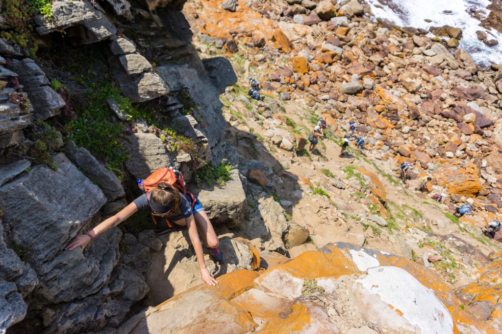 Klicken, um Bild zu vergrößern. Garden Route Südafrika - Auf einem Trek des Robberg Nature Reserve in Plettenberg Bay, klettert Sara ein paar Felsen hinauf.