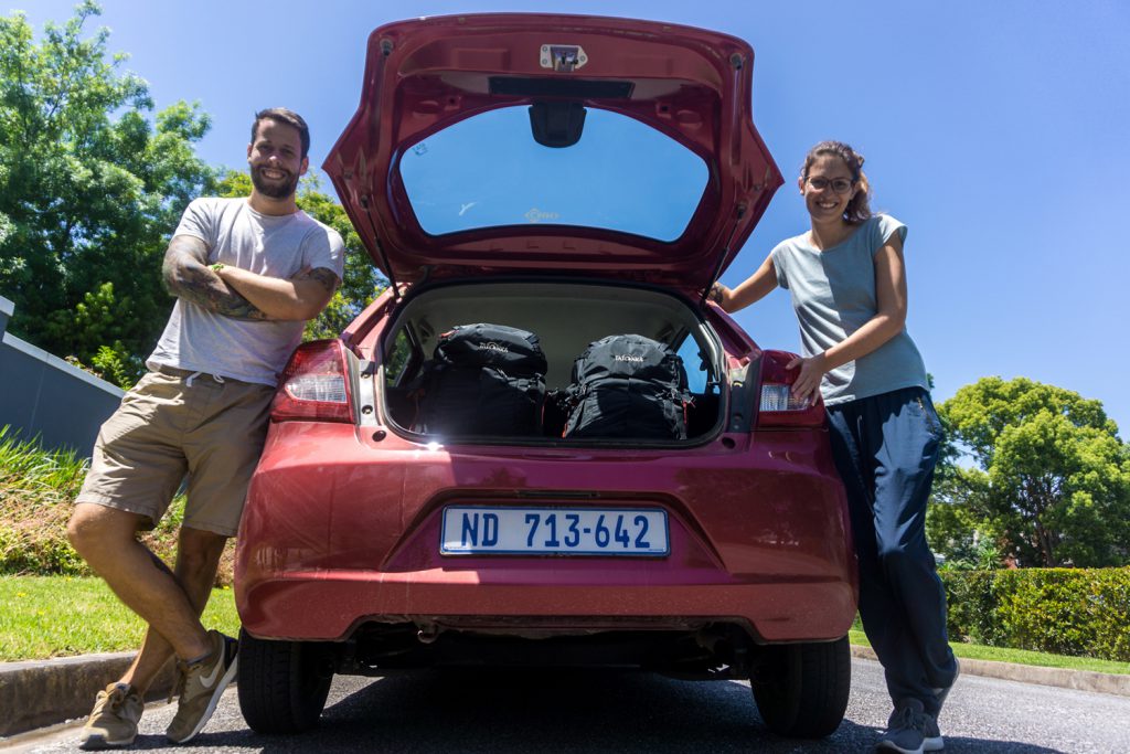 Garden Route Südafrika - Sara und Marco vor dem offenen Kofferraum ihres roten Mietwagens.