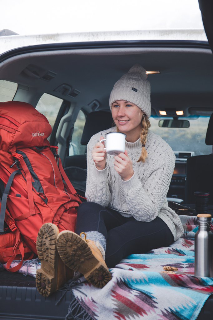 Line genießt eine Tasse Kaffee in ihrem Van während ihres Roadtrips durch Island.