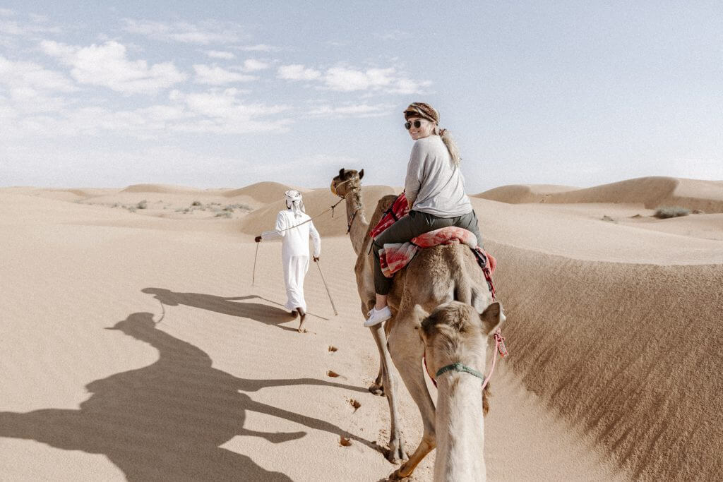 Joanna auf einem Kamel. Ein Beduine führt die Karawane durch die Wahiba Sands Wüste im Oman.