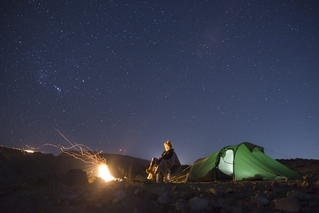 Kristallklarer Sternenhimmel über dem Oman – Joanna wärmt sich am Lagerfeuer vor ihrem Tatonka-Zelt.