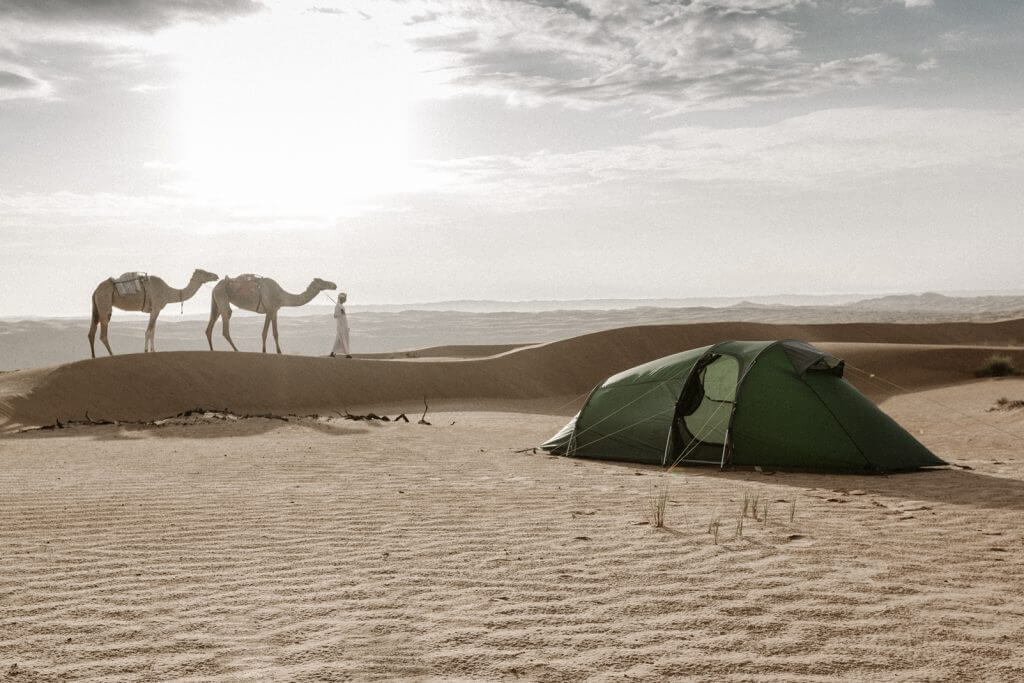 Aufgebautes Tatonka Zelt in der Wahiba Sands Wüste. Im Hintergrund zieht ein Beduine mit zwei Kamelen vorbei.